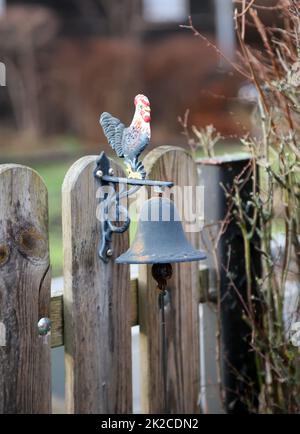 Una campana con un gallo su un cancello del giardino. Foto Stock