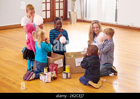 Mettendo sorrisi sui loro volti piccoli. Shot di un volontario che lavora con bambini piccoli. Foto Stock