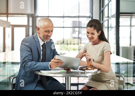 Occorre prendere decisioni importanti. Scatto corto di due uomini d'affari che lavorano insieme su un tablet digitale in un ufficio moderno. Foto Stock