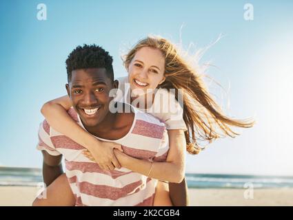 Non potete battere quella marca speciale dell'amore di estate. Scatto di una giovane coppia felice godendo un giro di piggyback alla spiaggia. Foto Stock