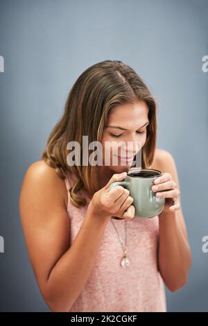 Il caffè fresco puzza Studio girato di una giovane donna che beve una tazza di caffè su uno sfondo grigio. Foto Stock