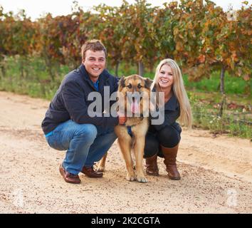 HES un membro della loro famiglia. Ritratto di una giovane coppia con il loro animale domestico alsaziano in una fattoria di vino. Foto Stock