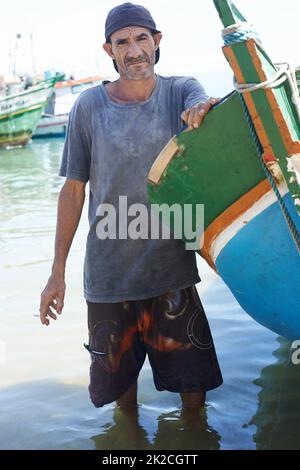 Essere un pescatore può essere duro. Ritratto di un pescatore in piedi in acque poco profonde accanto alla sua barca. Foto Stock