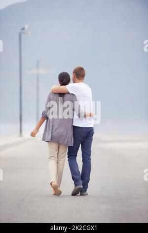 L'amore giovane è pieno di affetto. Foto retroversata a tutta lunghezza di una giovane coppia che cammina lungo una passeggiata. Foto Stock