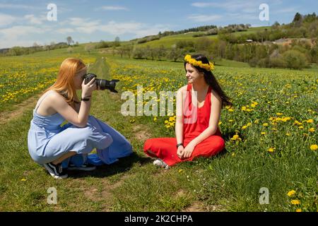 La ragazza giovane sta posando fotografando l'amico sul prato del dente di leone Foto Stock