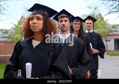 Istruzione superiore per alte aspirazioni. Shot di studenti universitari laureati in piedi in una fila guardando verso l'alto. Foto Stock