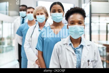 La qualità e la sicurezza sono il numero uno nel settore sanitario. Ritratto di un gruppo di medici che indossano maschere per il viso mentre si trova in piedi insieme in un ospedale. Foto Stock