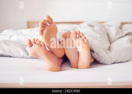 Lascia che rimanga a letto oggi. Shot di un piede di coppia che si aggancia da sotto un piumino. Foto Stock