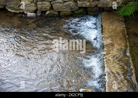 l'acqua si incanala su una vecchia diga di pietra nel vecchio canale Foto Stock