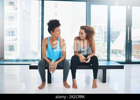 Lascia prendere un po 'di uno sfiatatoio. Ritratto girato di due giovani fit donne seduti su una panca e fare una chiacchierata prima di una sessione di yoga all'interno di uno studio. Foto Stock