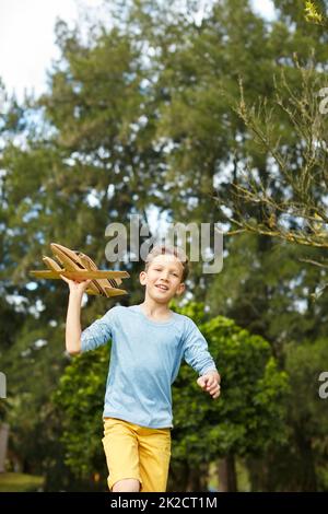 Prendere in aria. Shot di un ragazzo che corre attraverso un parco con un aeroplano giocattolo. Foto Stock