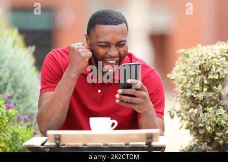 Uomo eccitato con il telefono di controllo della pelle nera in un bar Foto Stock