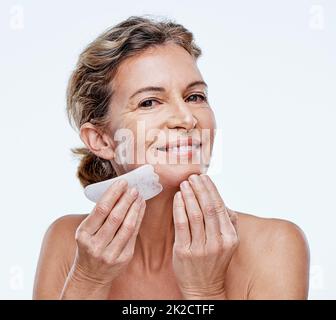 Funziona davvero. Scatto corto di una donna matura usando una qua Sha sul suo viso. Foto Stock