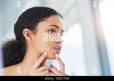 Le abitudini del BA muoiono duro. Scatto corto di una bella giovane donna che stringe un pimple nello specchio. Foto Stock