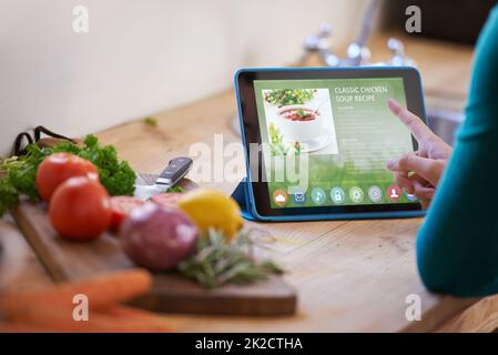 Ooh questo sembra bello.... Scatto corto di una giovane donna che guarda una ricetta online sul suo tablet digitale mentre prepara un pasto. Foto Stock