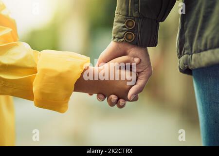 Tenere sempre le mani quando si attraversa la strada. Primo piano di un ragazzino irriconoscibile e di sua madre che tiene le mani sotto la pioggia all'esterno. Foto Stock