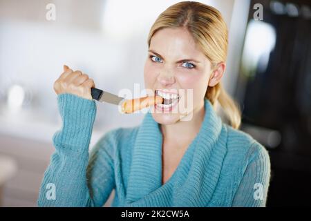 Dieting isnt per sissies. Ritratto di una bella giovane donna aggressivamente prendendo un morso da una carota. Foto Stock