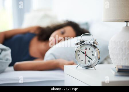 La sveglia, il ladro del miglior sonno. Scatto di una giovane donna attraente che si stendeva a letto con una sveglia sul suo comodino. Foto Stock