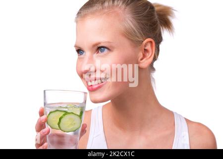 Zest per la vita. Scatto di una bella giovane donna con un bicchiere d'acqua con fette di cetriolo isolate su bianco. Foto Stock