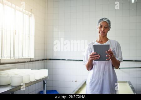 Ottenere un po 'di assistenza online. Scatto corto di una giovane lavoratrice di fattoria femminile utilizzando un tablet mentre si lavora in una fabbrica nella fattoria. Foto Stock