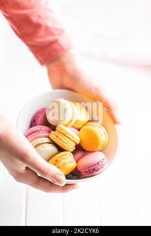 Amaretti colorati e dolci. Macaron francesi tradizionali. Gustoso dessert in ciotola tenuto in mano Foto Stock