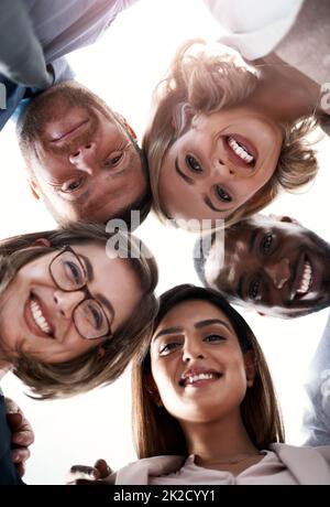 Siamo insieme e questo è ciò che rende un successo. Ritratto ad angolo basso di un gruppo di colleghi che guardano verso il basso la fotocamera mentre si trova in una capanne. Foto Stock