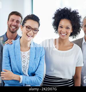 Lavoro di squadra con un sorriso. Ritratto di due colleghi che sorridono in ufficio con colleghi in background. Foto Stock