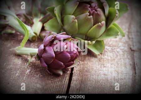 Carciofi viola sul rustico sfondo di legno Foto Stock