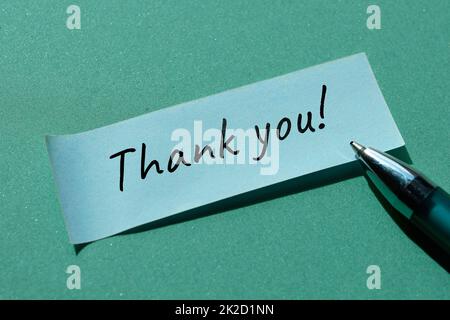 Messaggio grazie scritto su carta adesiva, adesivo per ufficio con penna. Nota scritta a mano semplice e minima su sfondo verde. Foto Stock
