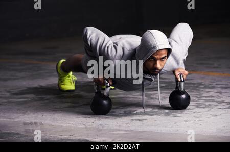 Concentrato sul suo allenamento. Colpo di un giovane che fa i push-up con i pesi della campana del bollitore. Foto Stock