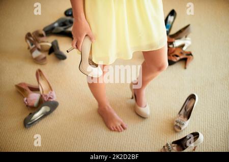 Trovare un equilibrio tra stile e comfort. Immagine ritagliata di una donna in piedi nella sua stanza circondata da scarpe. Foto Stock