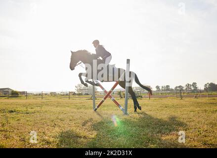 Ho addestrato per questo. Scatto di un giovane cavaliere che salta sopra un ostacolo sul suo cavallo. Foto Stock