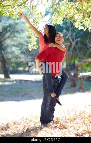 Divertirsi all'aperto insieme. Scatto di un bel giovane uomo che dà alla sua ragazza una cavalcata di piggyback nel parco. Foto Stock