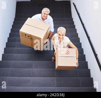 Fai il passo per ricordi nuovi di zecca. Scatto di una coppia matura che porta le scatole sulle scale in un giorno in movimento. Foto Stock