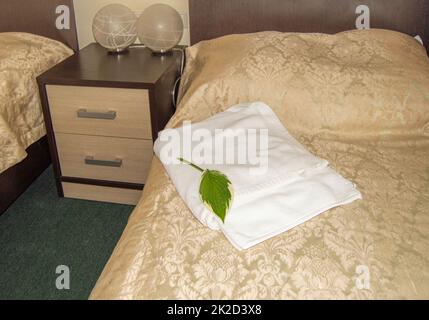 Gli interni di un hotel moderno, un letto con un cuscino e un lussuoso copriletto dorato e asciugamani bianchi, lampade di design sul comodino Foto Stock