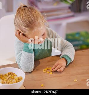 Non mi piace questo cereale. Scatto di una ragazza piccola che osserva triste mentre mangiano la colazione a casa. Foto Stock