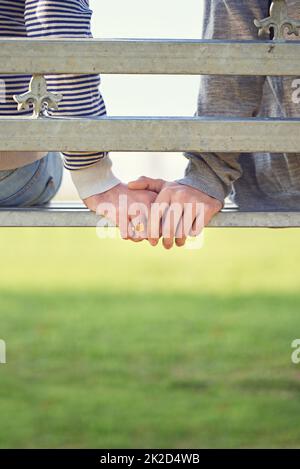 Sempre a portata di mano. Ripresa retroguarata di una giovane coppia gay seduta insieme su una panchina del parco. Foto Stock