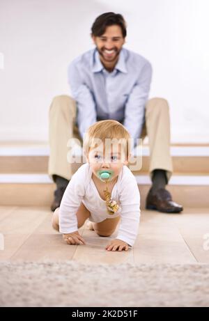 Guardalo andare. Un bel padre che guarda il suo bambino che strisciare. Foto Stock