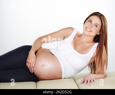 La shes ha ottenuto quel bagliore di gravidanza. Scatto corto di una donna incinta che tiene il suo ventre mentre si rilassa. Foto Stock