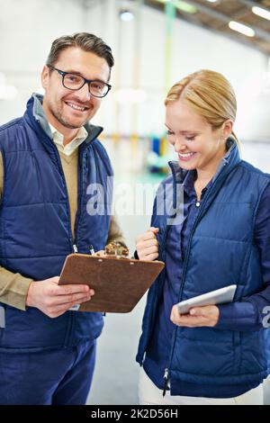 Its always good to have a hard copy. two people looking at paperwork while working in a warehouse. Foto Stock