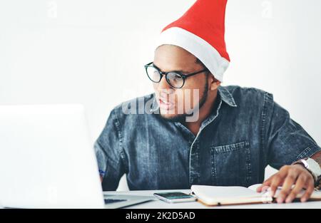 Babbo Natale potrebbe usare un piccolo aiutante in giro ora. Scatto corto di un bel giovane uomo d'affari che lavora nel suo ufficio la vigilia di Natale. Foto Stock
