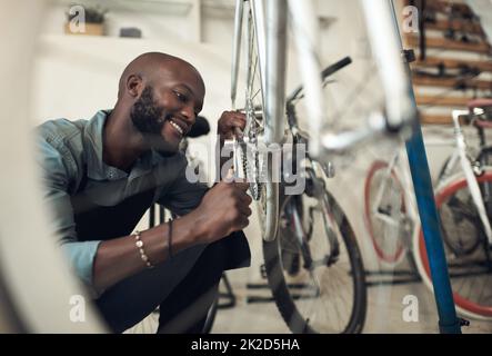 Im quasi fatto risolvere questo. Scatto di un bel giovane uomo accovacciato da solo nel suo negozio e riparare una ruota di bicicletta. Foto Stock