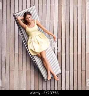 Rilassante nello stile. Una donna giovane e ricca che si trova sul suo lettino in un abito estivo. Foto Stock