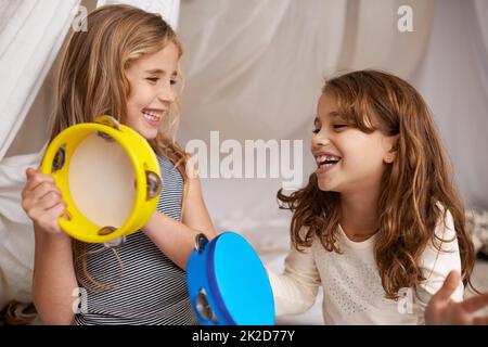 Musica e gioia. Scatto di due ragazze piccole carine che giocano con i tamburini a casa. Foto Stock