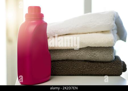 Chi non ama gli asciugamani puliti. Shot di una bottiglia di detergente insieme a una pila di asciugamani piegati a casa. Foto Stock