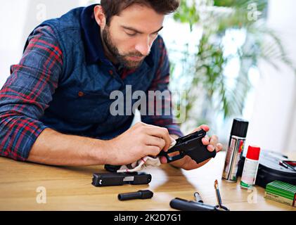 La manutenzione regolare è essenziale per ogni proprietario di pistola. Un giovane pulisce la pistola. Foto Stock