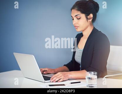 Lavorare diligentemente. Scatto corto di una giovane donna d'affari attraente che lavora su un laptop nel suo ufficio. Foto Stock