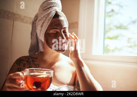 Trattatevi come se trattiate gli altri. Scatto di una giovane donna che ha il tè mentre si dà un viso a casa. Foto Stock