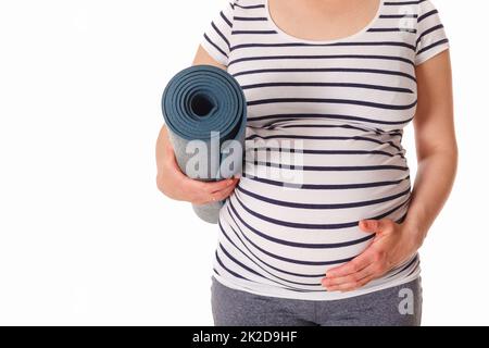 Donna incinta in piedi con tappeto yoga Foto Stock