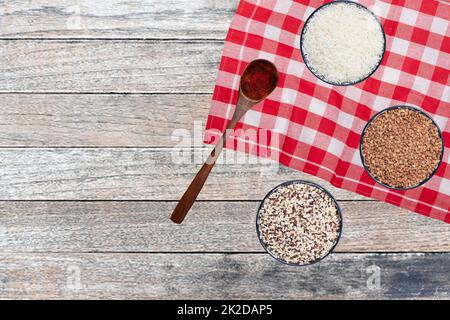 Cibo vegetale. Primo piano di tre ciotole con riso, grano saraceno e quinoa e un cucchiaio con fili di spezie safran su tavolo sfocato astratto. Mangiare sano. Vista dall'alto con lo spazio. Foto Stock